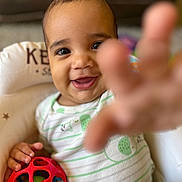 Milo is registered to the contest to win money with this photo: baby, child, smiling, toy, red_ball, hand, face, cushion, infant, clothing, playful, indoor, person, closeup, happy, seat, baby_chair, cute, young_child, portrait