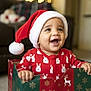 Milo is registered to the contest to win money with this photo: baby, child, santa_hat, christmas, holiday, gift_box, pajamas, bunny_pattern, smiling, happy, indoors, bokeh, festive, red_clothing, celebration, cute, seasonal, face, person, joyful