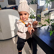 Milo joined the competition — help win amazing prizes! bear_design, black_pants, chair, child, floor, home, indoor, knit_hat, leafy_plant, living_room, person, plant, pom_pom, shadow, socks, sunlight, sweater, table, toddler, window