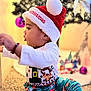 Milo is registered to the contest to win money with this photo: celebration, child, christmas_pajamas, christmas_tree, colorful_clothing, cute, decorations, festive, fun, holiday, holiday_season, home, indoor, person, red_hat, santa_hat, seasonal, smiling, toddler, young_child