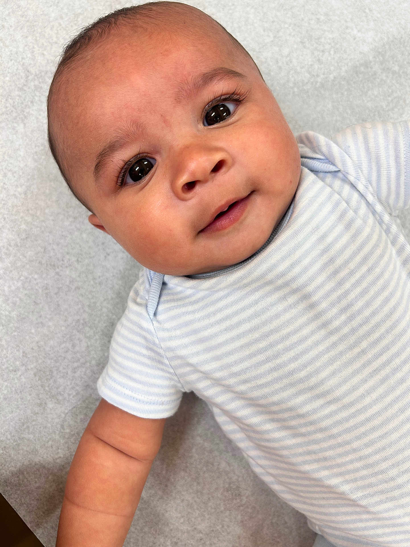 Marley is registered to the contest to win money with this photo: baby, infant, face, eyes, smile, onesie, striped_clothing, skin, arm, head, closeup, portrait, child, young, cute, lying_down, expression, baby_clothes, human, soft_background