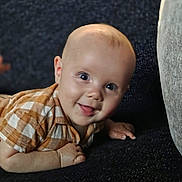 Jace is registered to the contest to win money with this photo: baby, child, smiling, face, head, eyes, mouth, tongue, shirt, clothing, checkered, pattern, skin, hand, fingers, lying_down, crawling, indoors, portrait, happy