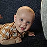 baby, child, smiling, face, head, eyes, mouth, tongue, shirt, clothing, checkered, pattern, skin, hand, fingers, lying_down, crawling, indoors, portrait, happy