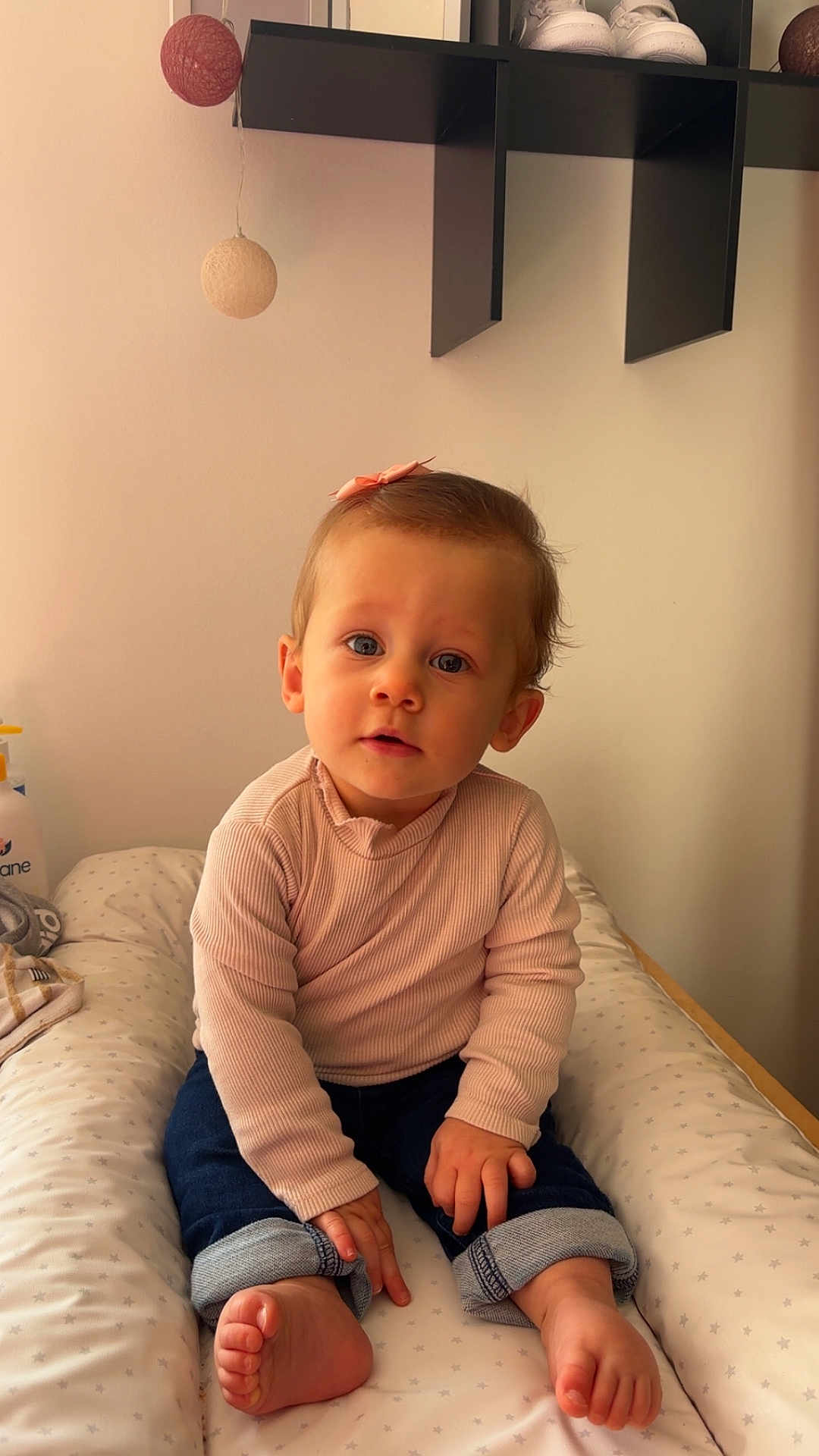 Inaya a rejoint le concours — aidez-le/la à gagner de superbes lots ! toddler, child, baby, sitting, pink_top, jeans, barefoot, bow, curly_hair, cushion, decor, shelf, shoes, indoor, minimalist, portrait, cute, curious, soft_lighting, face