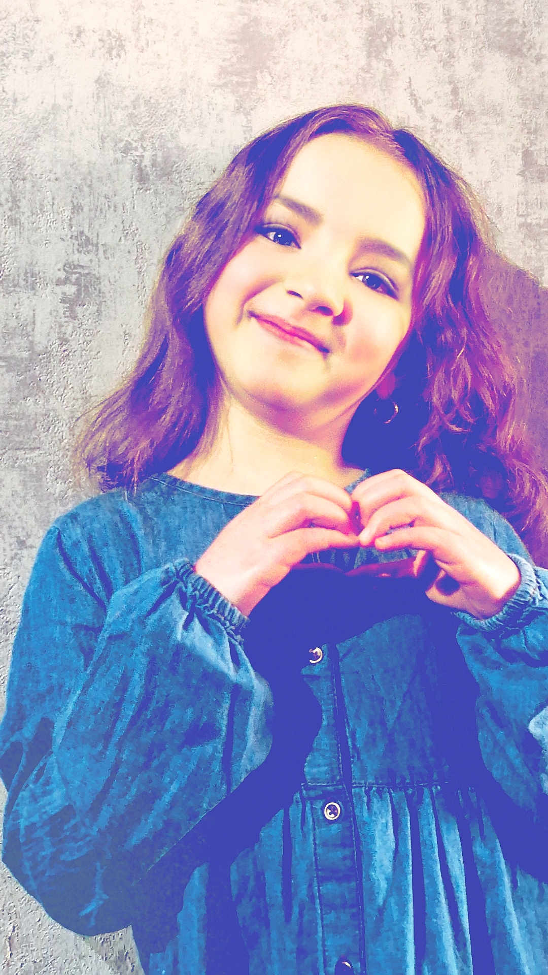Kendra participe au concours pour gagner de l'argent avec cette photo : child, girl, smiling, hand_gesture, heart_shape, blue_dress, long_hair, portrait, happy, standing, wall, texture, casual_clothing, indoor, young, cute, person, fashion, gesture, expression