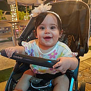 Charlotte is registered to the contest to win money with this photo: baby, child, stroller, smiling, flower_headband, colorful_clothing, outdoor, night, lights, umbrella, happy, person, infant, cute, seatbelt, polka_dot, hand, face, expression, footwear
