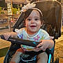 baby, child, stroller, smiling, flower_headband, colorful_clothing, outdoor, night, lights, umbrella, happy, person, infant, cute, seatbelt, polka_dot, hand, face, expression, footwear