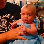 Tony is registered to the contest to win money with this photo: baby, child, adult, blanket, blue_blanket, holding, indoor, video_call, screen_inset, smile, person, face, hand, clothing, shirt, skeleton_design, furniture, room, window, curtain