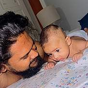 Thabit joined the competition — help win amazing prizes! baby, man, bed, floral_bedspread, face, beard, curly_hair, indoor, room, lamp, door, skin, close_up, portrait, interaction, parent_and_child, tender_moment, lying_down, expression, looking