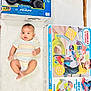 Thabit is registered to the contest to win money with this photo: baby, infant, toy_box, remote_control_car, train_table, striped_onesie, white_background, floor, child, indoor, playtime, cute, young_child, colorful_toys, lying_down, soft_surface, packaging, product_boxes, curious, adorable