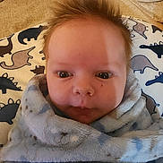 Keith is registered to the contest to win money with this photo: baby, infant, face, blanket, soft_fabric, dinosaur_pattern, hair, cute, wrapped, indoors, closeup, child, portrait, cozy, expression, newborn, person, skin, head, comfort