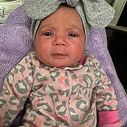 Hannah is registered to the contest to win money with this photo: baby, bow, child, clothing, cozy, expression, face, furniture, headband, home, indoor, infant, leopard_print, newborn, onesie, person, photograph, pink, portrait, purple_blanket