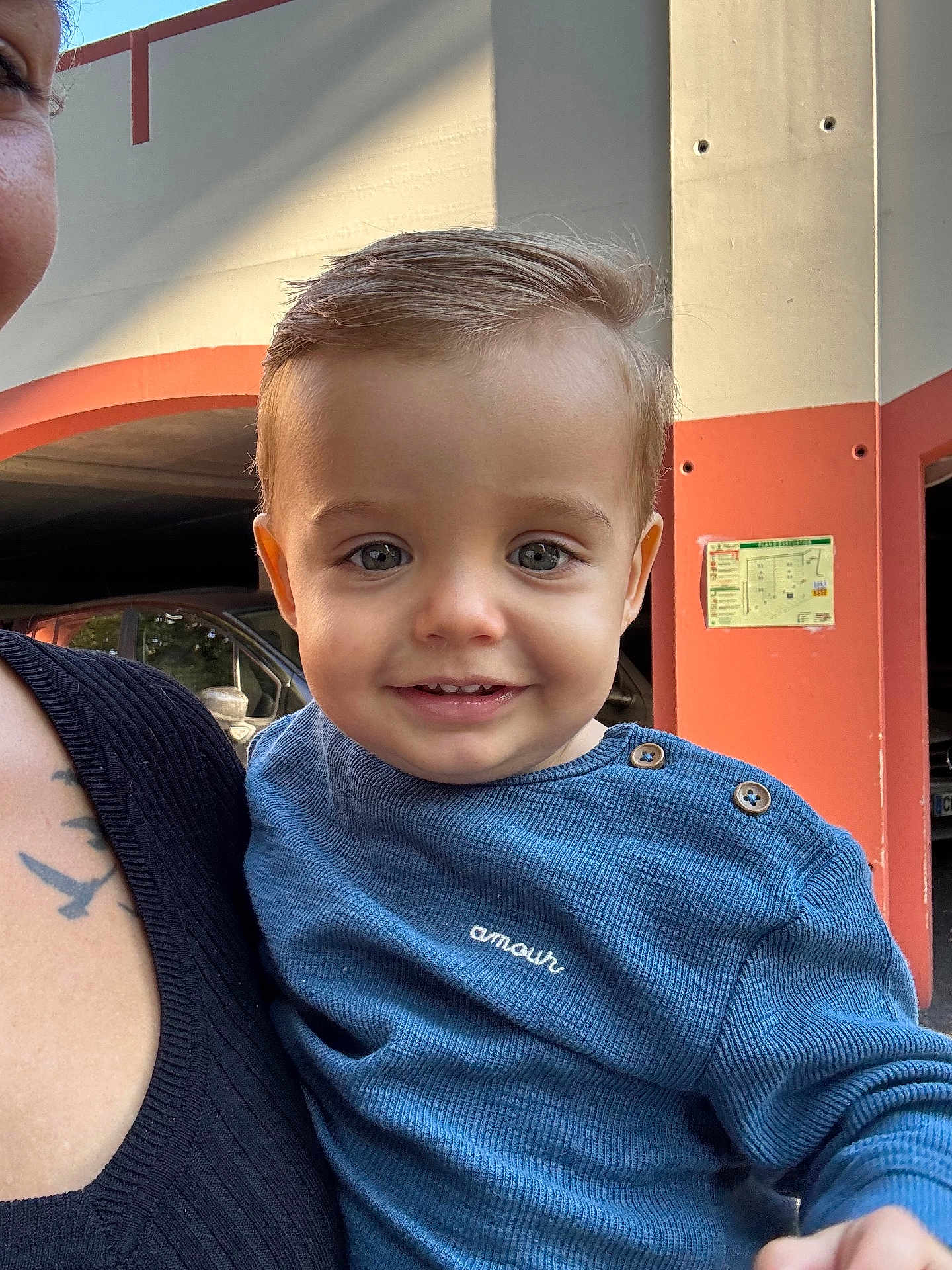 Hugo a rejoint le concours — aidez-le/la à gagner de superbes lots ! toddler, child, smile, face, blue_sweater, buttons, amour, adult, tattoo, shoulder, urban, background, car, parking_garage, person, portrait, daylight, holding, happy, closeup