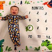 Benjamin is registered to the contest to win money with this photo: baby, blanket, celebration, child, clothing, colorful, cute, dinosaur, fabric, green, happy, infant, lying_down, milestone, months, number, pajamas, pattern, playful, smiling