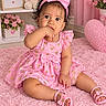 baby, child, toddler, portrait, sitting, pink, dress, bow, headband, smiling, face, curly_hair, baby_shoes, rug, flowers, teddy_bear, bedroom, indoors, floral_decor, heart_pattern