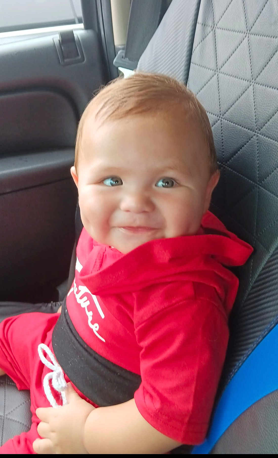 Joshua is registered to the contest to win money with this photo: baby, child, car_seat, red_clothing, smile, dimples, indoor, seatbelt, cute, person, young_child, portrait, sitting, car_interior, clothing, hoodie, hand, face, happy, infant