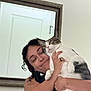Swisher joined the competition — help win amazing prizes! person, cat, indoor, mirror, tattoo, smiling, curly_hair, white_wall, black_clothing, holding, pet, affection, domestic_animal, face, hand, feline, close_up, portrait, happy, home