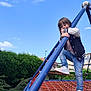 active, blue_sky, casual_clothing, child, climbing, daylight, fun, greenery, happy, jeans, outdoor, park, play, playground, recreation, rope_structure, smiling, sneakers, sporty_jacket, young