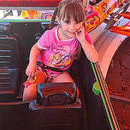 Capucine participe au concours pour gagner de l'argent avec cette photo : child, girl, braids, pink_clothing, paw_patrol, amusement_ride, seatbelt, ride_car, colorful, playful, smiling, finger_in_mouth, card, daylight, outdoor, entertainment, fun, seat, person, hair