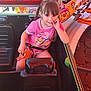 child, girl, braids, pink_clothing, paw_patrol, amusement_ride, seatbelt, ride_car, colorful, playful, smiling, finger_in_mouth, card, daylight, outdoor, entertainment, fun, seat, person, hair