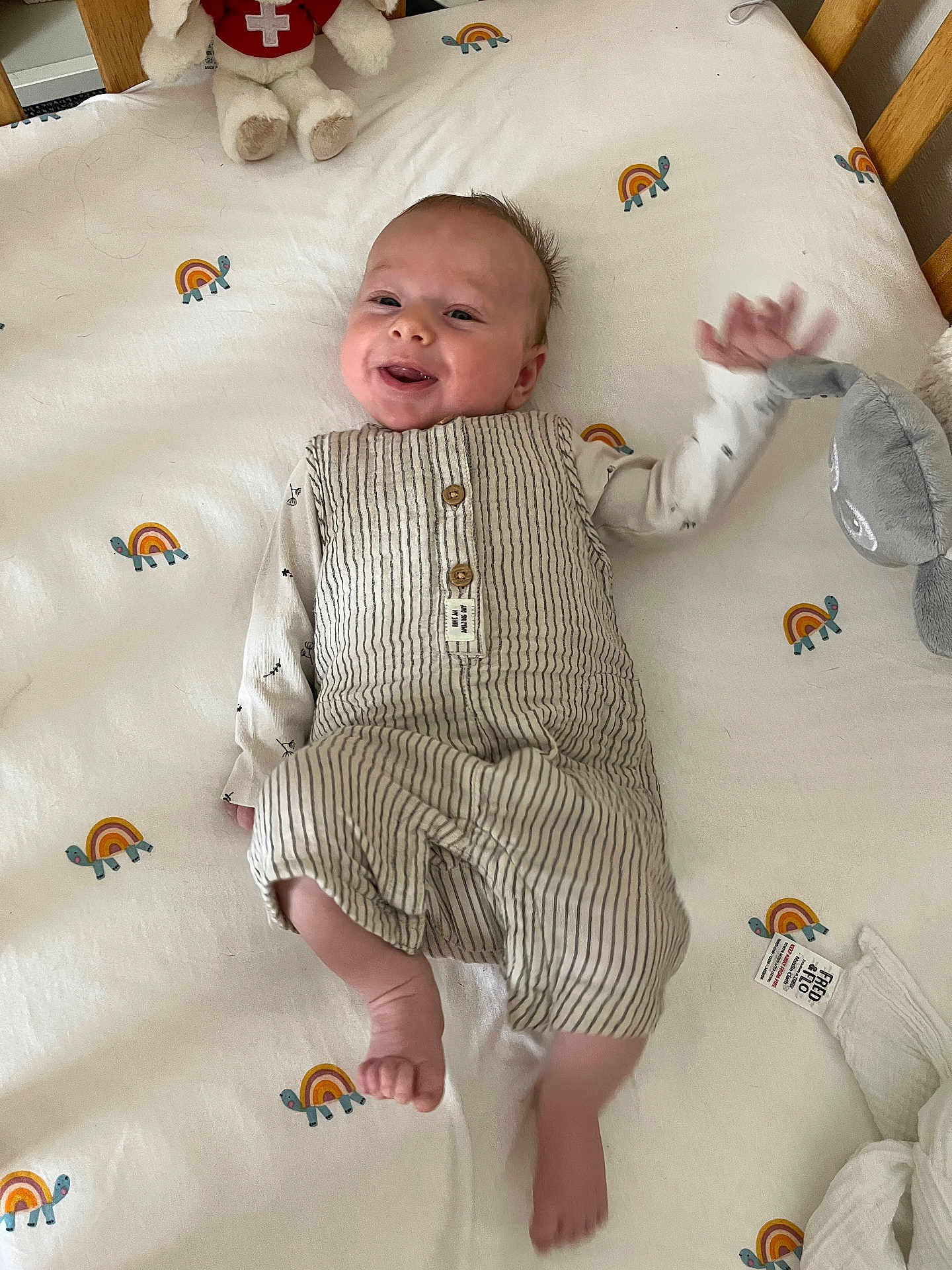 August joined the competition — help win amazing prizes! baby, infant, smiling, striped_clothing, white_sheet, turtle_pattern, plush_toy, crib, wooden_rail, waving_hand, foot, happy, lying_down, cute, child, room, soft_toy, blanket, sleepwear, indoors