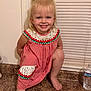 toddler, child, smiling, blonde_hair, dress, red_and_white, kitchen_counter, barefoot, window_blinds, water_bottle, indoor, happy, cute, portrait, person, flooring, playful, crouching, clothing, hair_tied