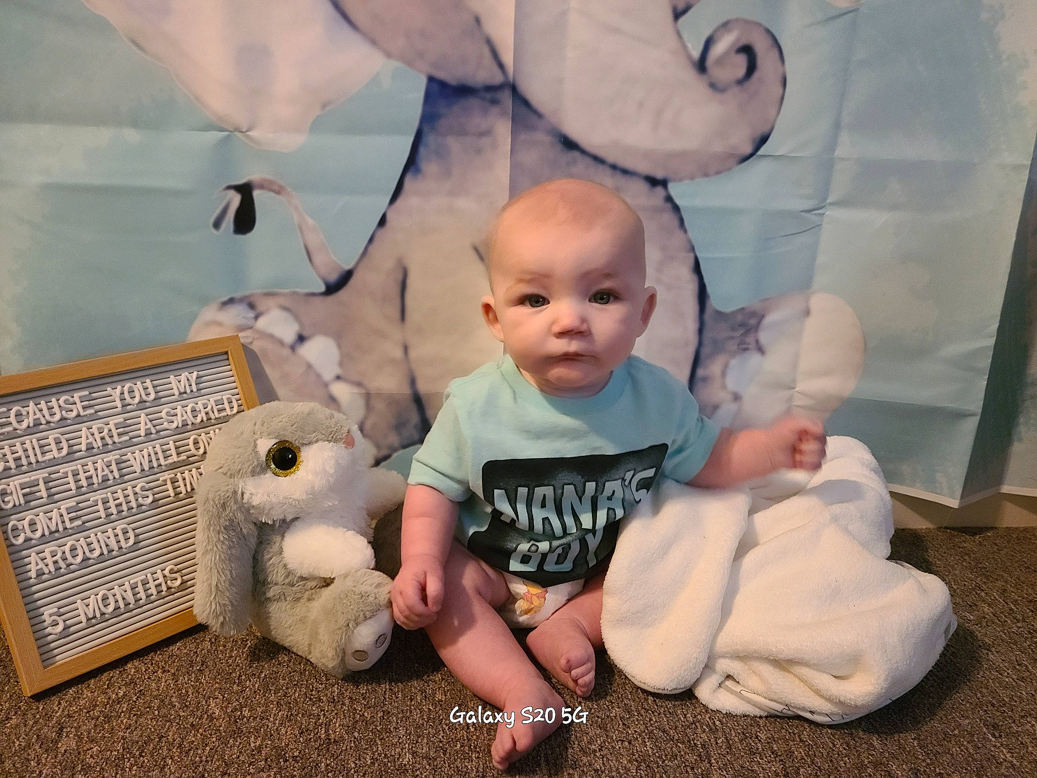 Everett is registered to the contest to win money with this photo: baby, baby_toddler_clothing, child, comfort, flooring, fun, grass, happy, person, room, sandal, sitting, skin, sock, t_shirt, toddler, wood