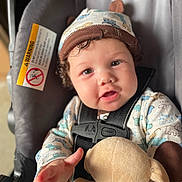 Maverick is registered to the contest to win money with this photo: baby, child, car_seat, curly_hair, hat, pajamas, plush_toy, reaching_hand, seatbelt, smiling, cute, indoors, portrait, infant, child_seat, animal_print, child_clothing, baby_face, baby_hat, soft_toy