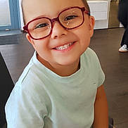Noam participe au concours pour gagner de l'argent avec cette photo : child, boy, glasses, smile, indoor, eyewear_store, furniture, person, short_hair, casual_clothing, light_blue_shirt, happy, seated, modern_interior, flooring, retail, spectacles, face, portrait, cute