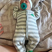Edward is registered to the contest to win money with this photo: baby, infant, child, portrait, lying_down, pacifier, onesie, striped_clothing, hat, green, dinosaur_socks, couch, blanket, fabric, indoor, cozy, face, sleepy, photography, baby_clothing