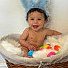 Liam is registered to the contest to win money with this photo: baby, bunny_ears, basket, colorful_eggs, smiling, happy, fur_lining, indoor, cute, child, infant, playful, toy, headwear, person, portrait, sitting, wicker, cheerful, young_child