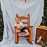 baby, backdrop, bow_tie, child, crate, fabric, greenery, leaves, outdoor, photography, portrait, props, rocking_chair, shoes, sitting, smile, stuffed_bunny, toddler, toy_carrot, wooden_chair