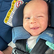 Jace is registered to the contest to win money with this photo: baby, blue, car_seat, child, closeup, clothing, cute, fabric, happy, indoors, infant, person, portrait, safety_harness, seat, seatbelt, smiling, tongue_out, warning_label, winking