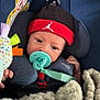 Jace is registered to the contest to win money with this photo: baby, beanie, blanket, car_seat, child, closeup, clothing, comfort, cushion, cute, face, headwear, indoor, infant, pacifier, person, rest, seatbelt, toy, warm
