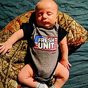 Dean is registered to the contest to win money with this photo: baby, sleeping, onesie, clothing, blanket, camouflage, blue, bed, infant, child, cute, peaceful, sock, lying_down, indoor, portrait, skin, newborn, hand, footwear
