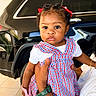 toddler, child, baby, plaid_dress, red_bows, toy, hand, watch, car, black_car, outdoor, person, face, curly_hair, earrings, white_shirt, holding, expression, portrait, floor