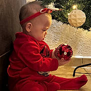 Mélina participe au concours pour gagner de l'argent avec cette photo : baby, child, christmas_ornament, christmas_tree, curious, cute, decorations, festive, floor, headband, holiday, holiday_season, indoor, lighting, person, red_clothing, seated, tiled_floor, toy, wall