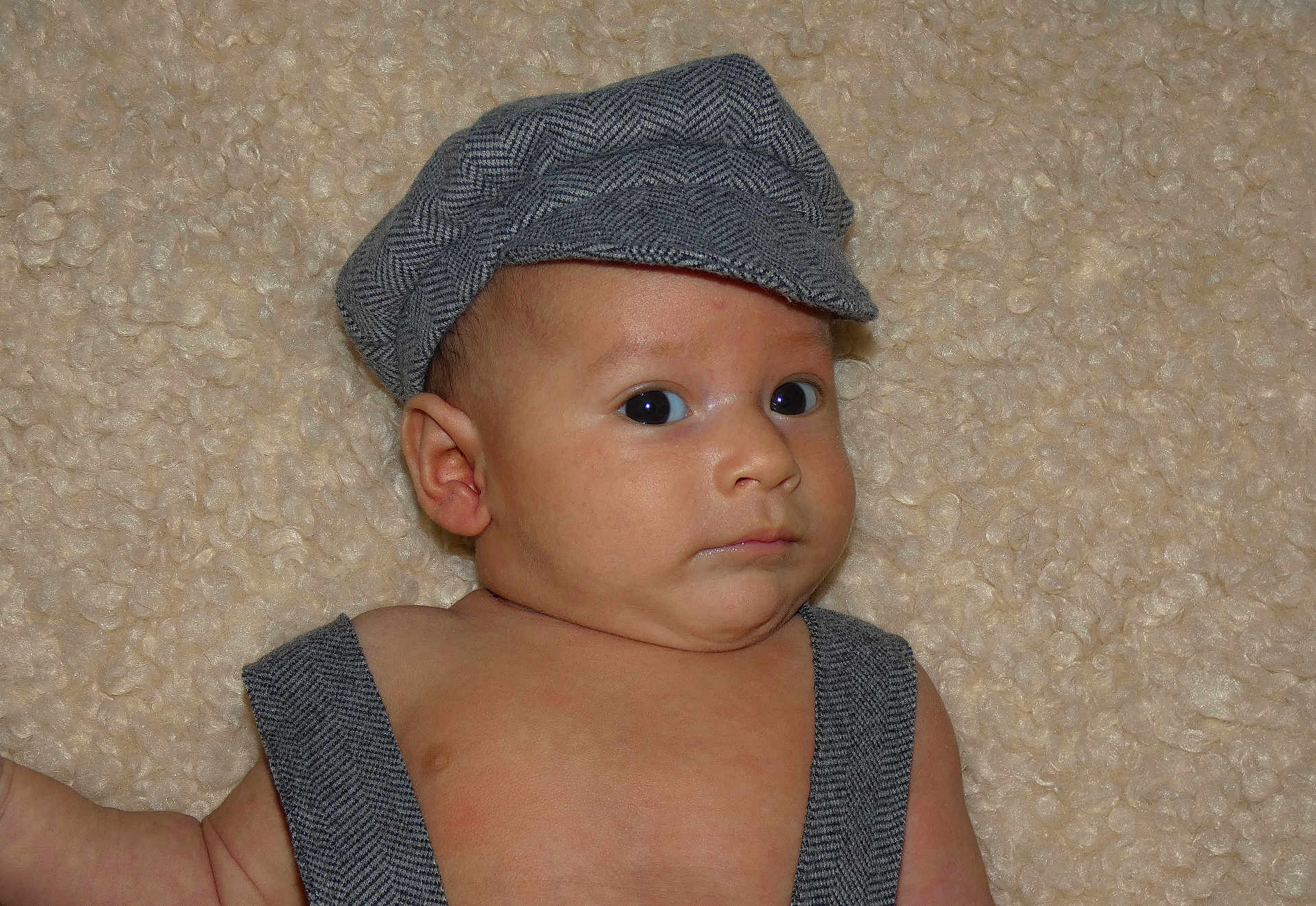 Isaac participe au concours pour gagner de l'argent avec cette photo : baby, infant, face, cap, clothing, suspenders, skin, expression, lying_down, blanket, texture, cute, child, young, portrait, indoor, headwear, human, person, looking