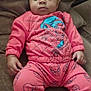 baby, child, infant, couch, brown_couch, pink_clothing, spiderman, onesie, baby_clothes, face, hands, feet, sitting, indoors, cushion, soft_furniture, relaxed, looking_down, portrait, person