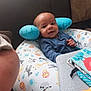 baby, infant, cushion, animal_print, blue_pillow, smile, face, child, indoor, sofa, book, toy, cozy, cute, person, pattern, fabric, home, relaxing, comfort