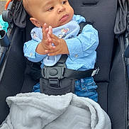 Wyatt is registered to the contest to win money with this photo: baby, stroller, blanket, blue_shirt, mickey_mouse, bib, hands, clasped_hands, infant, face, expression, jeans, straps, seat, outdoor, pavement, cute, child, person, portrait