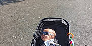Wyatt is registered to the contest to win money with this photo: baby, baby_bottle_holder, child, fan, infant, leisure, outdoor, park, pavement, person, plaything, relaxation, shade, stroller, summer, sunglasses, sunny, toy, tree, water