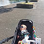 baby, stroller, sunglasses, outdoor, sunny, water, pavement, tree, toy, fan, child, shade, park, relaxation, infant, plaything, baby_bottle_holder, summer, leisure, person