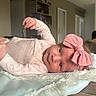baby, infant, pink_bow, headband, blanket, wooden_table, indoors, face, clothing, cute, lying_down, soft_texture, curious_eyes, child, portrait, newborn, baby_girl, room, home, casual