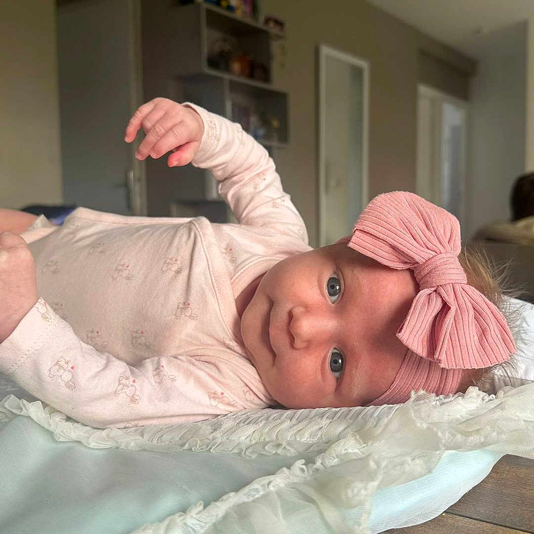 Lysie participe au concours pour gagner de l'argent avec cette photo : baby, infant, pink_bow, headband, blanket, wooden_table, indoors, face, clothing, cute, lying_down, soft_texture, curious_eyes, child, portrait, newborn, baby_girl, room, home, casual