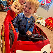 Huntley joined the competition — help win amazing prizes! child, toddler, toy_car, red, lightning_mcqueen, steering_wheel, pajamas, carpet, blanket, room, indoor, smile, play, fun, curly_hair, blonde_hair, face, person, car, kids_room