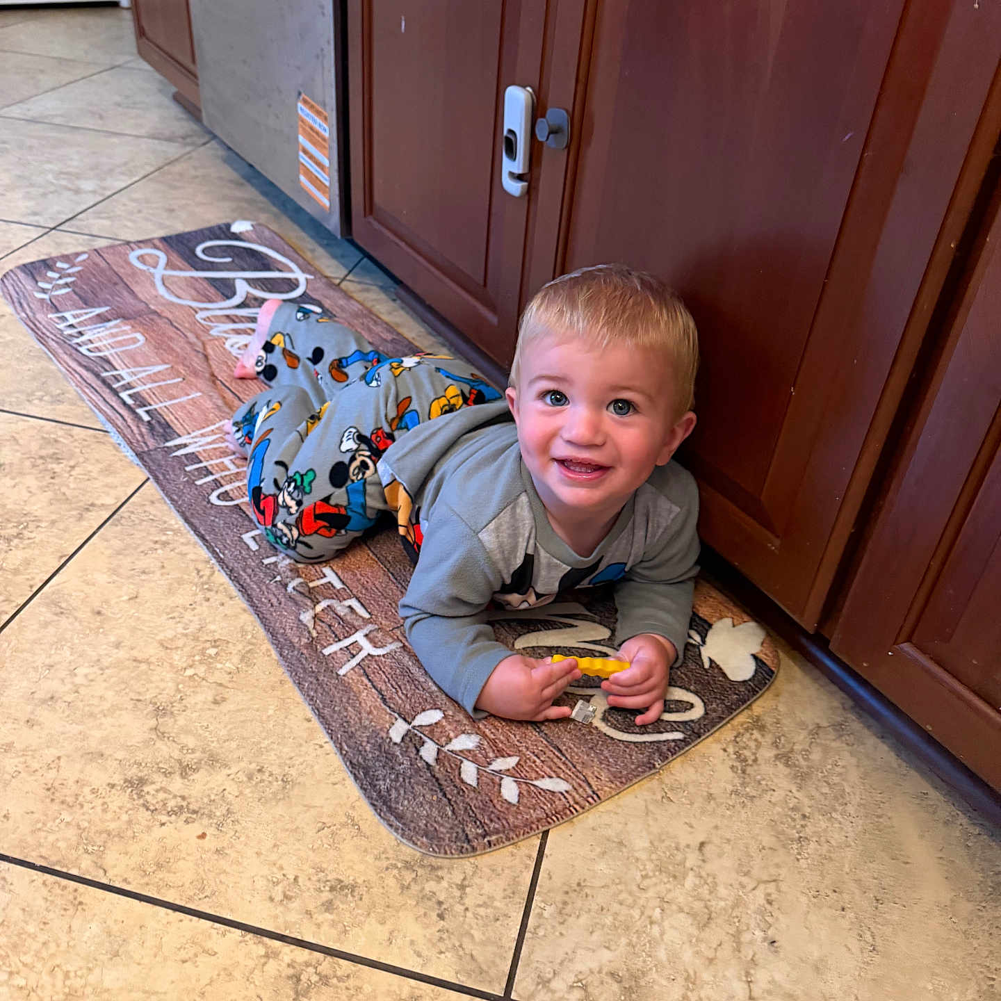 Huntley joined the competition — help win amazing prizes! toddler, child, smiling, pajamas, toy, floor, kitchen, mat, cabinet, wooden_cabinet, tile_floor, indoor, happy, person, young_child, playful, cute, home, portrait, lying_down