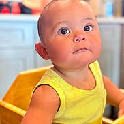 Denyer David Corona is registered to the contest to win money with this photo: toddler, child, face, eyes, yellow_tank_top, high_chair, wooden_furniture, indoor, kitchen, curious, expression, skin, person, portrait, baby, cute, sitting, closeup, young_child, bright