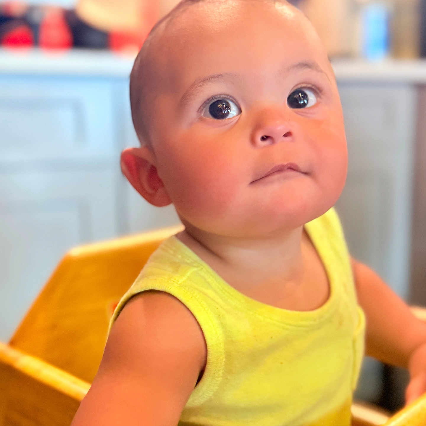Denyer David Corona is registered to the contest to win money with this photo: baby, bright, child, closeup, curious, cute, expression, eyes, face, high_chair, indoor, kitchen, person, portrait, sitting, skin, toddler, wooden_furniture, yellow_tank_top, young_child