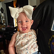 Lilith joined the competition — help win amazing prizes! baby, child, smiling, bow, headwear, floral_top, denim_shorts, indoor, person, holding, happy, face, cute, infant, clothing, portrait, home, furniture, curtains, light